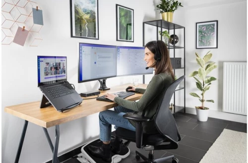 kobieta pracująca przy biurku, siedząca na ergonomicznym krześle biurowym, trzymająca stopy na podnóżku