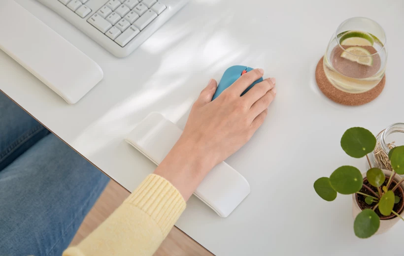 kobieca dłoń oparta o umieszczoną na biurku podkładkę, trzymająca w ręku myszkę komputerową