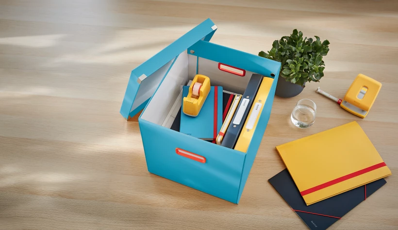 niebieskie pudełko z otwartą pokrywą i umieszczonymi wewnątrz akcesoriami, leżące na biurku 