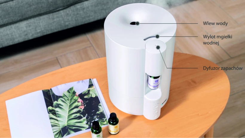 nawilżacz powietrza Blaupunkt AHA50 stojący na stoliku kawowym, z oznaczeniem wlewu wody, wylotu mgiełki oraz dyfuzora zapachów